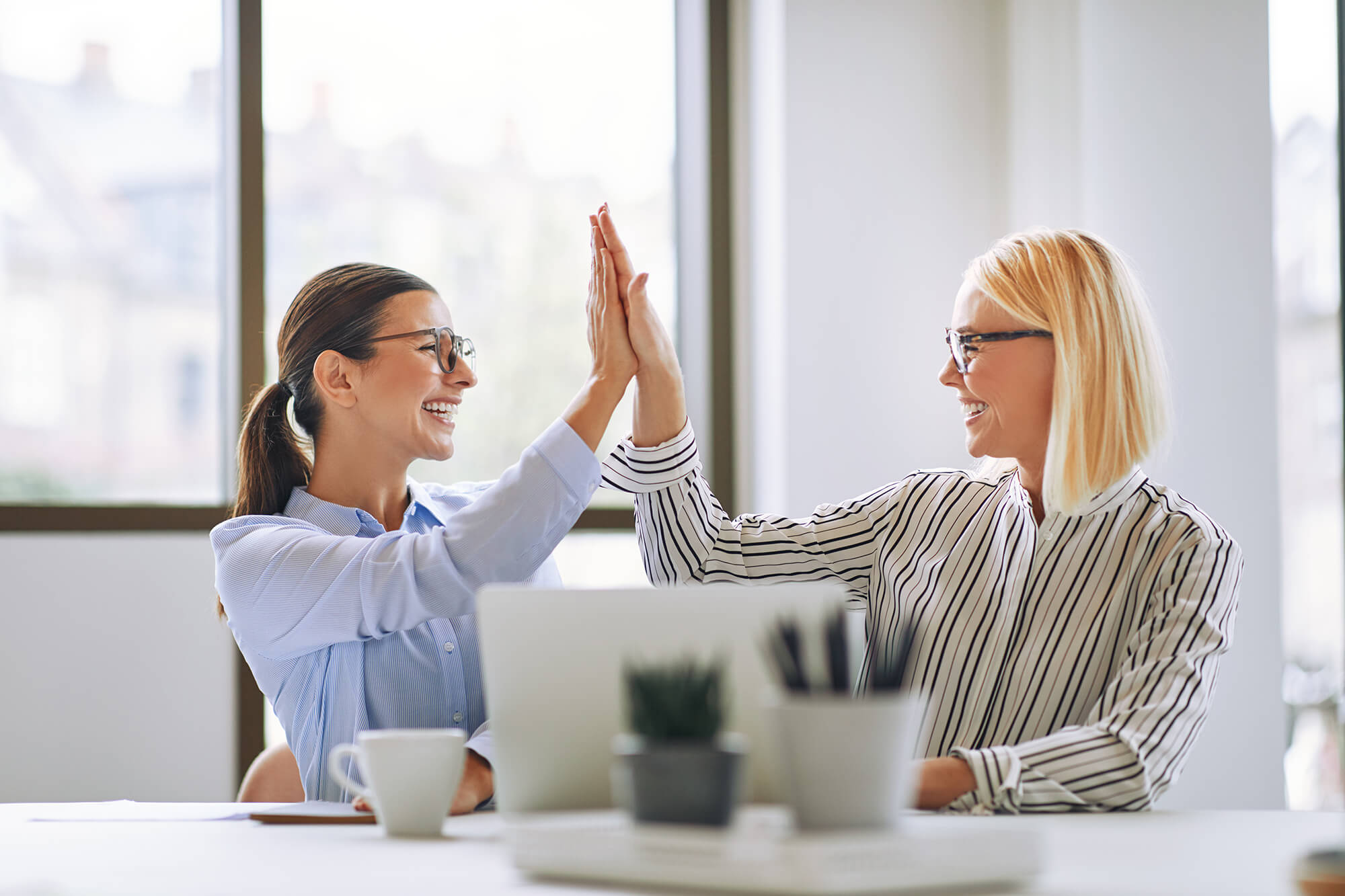 two-smiling-businesswomen-high-fiving-together-in-DDNACN5-1.jpg
